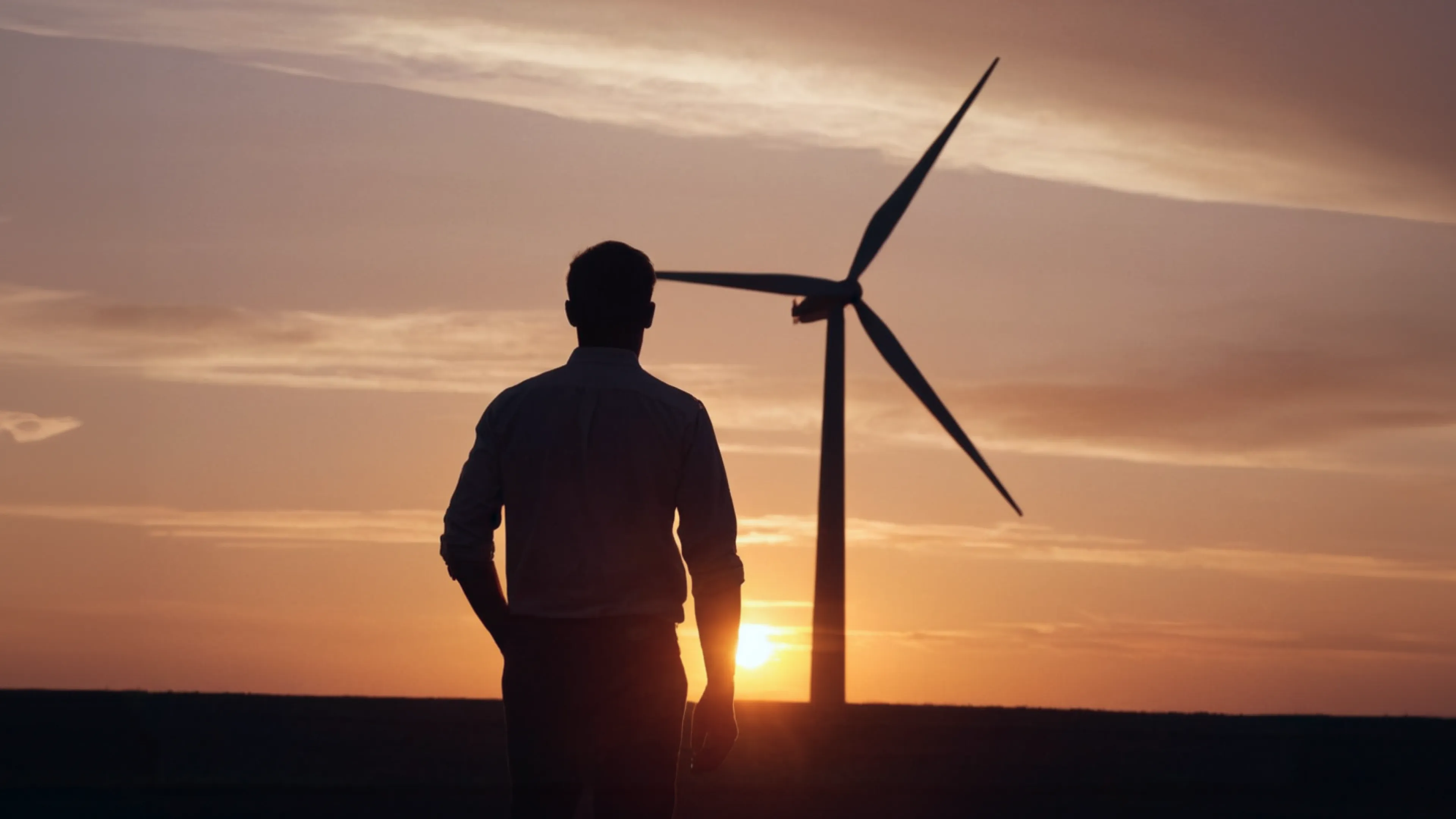 석양 속 풍력발전소를 바라보는 성인 남성의 희망적인 뒷모습 이미지